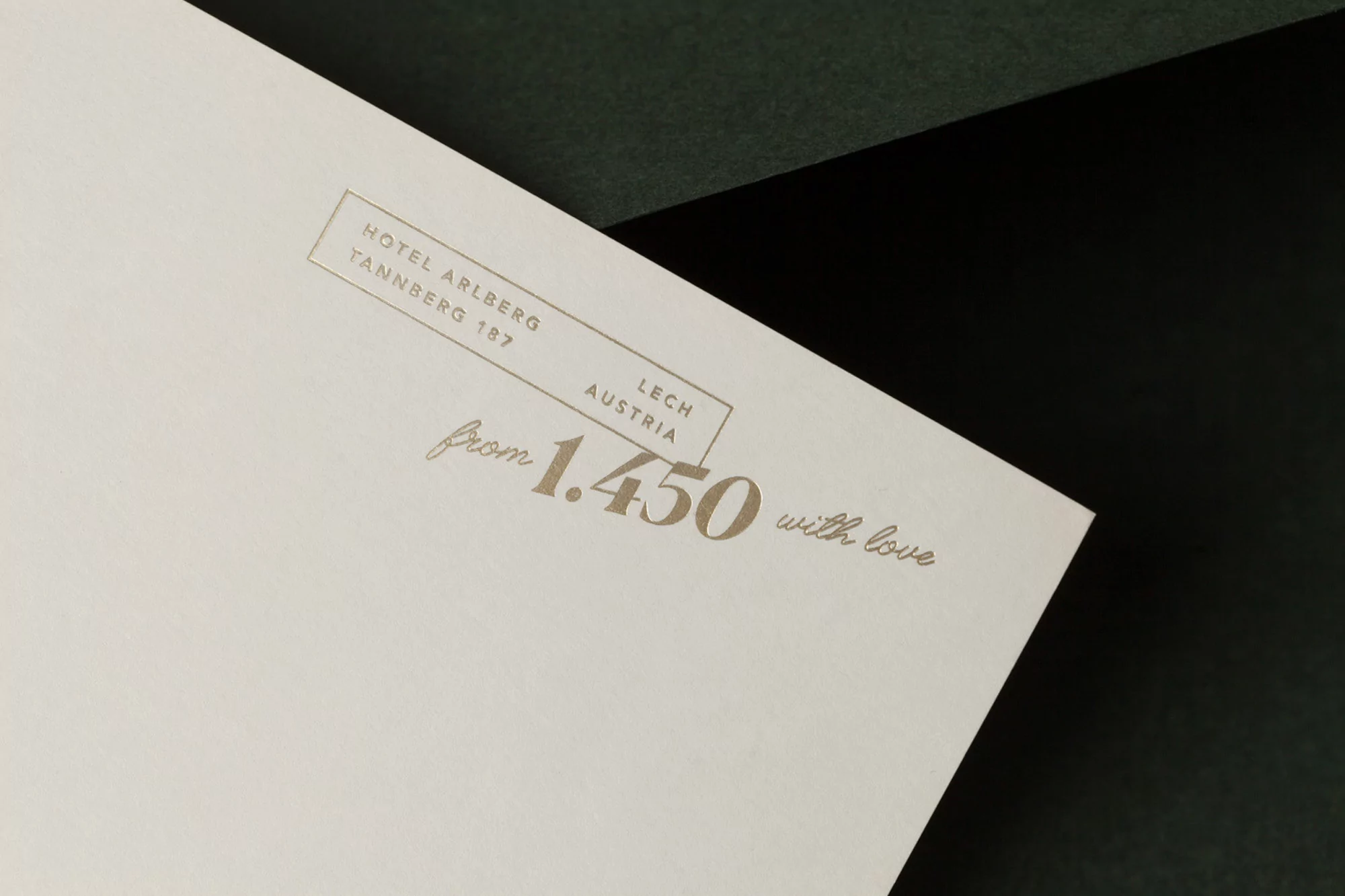 Close-up of an off-white card featuring gold lettering, including hotel information, the location, and the phrase 'from 1.450 with love'.