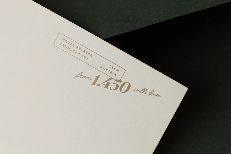 Close-up of an off-white card featuring gold lettering, including hotel information, the location, and the phrase 'from 1.450 with love'.