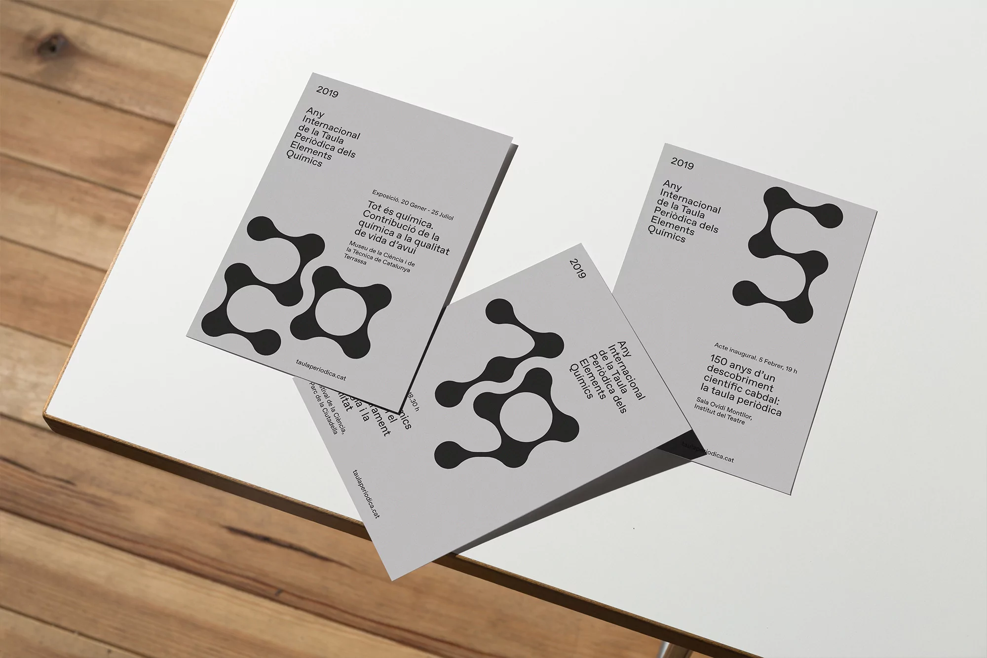 Three grey posters on a white table advertise the International Year of the Periodic Table of Elements, featuring a molecule graphic.