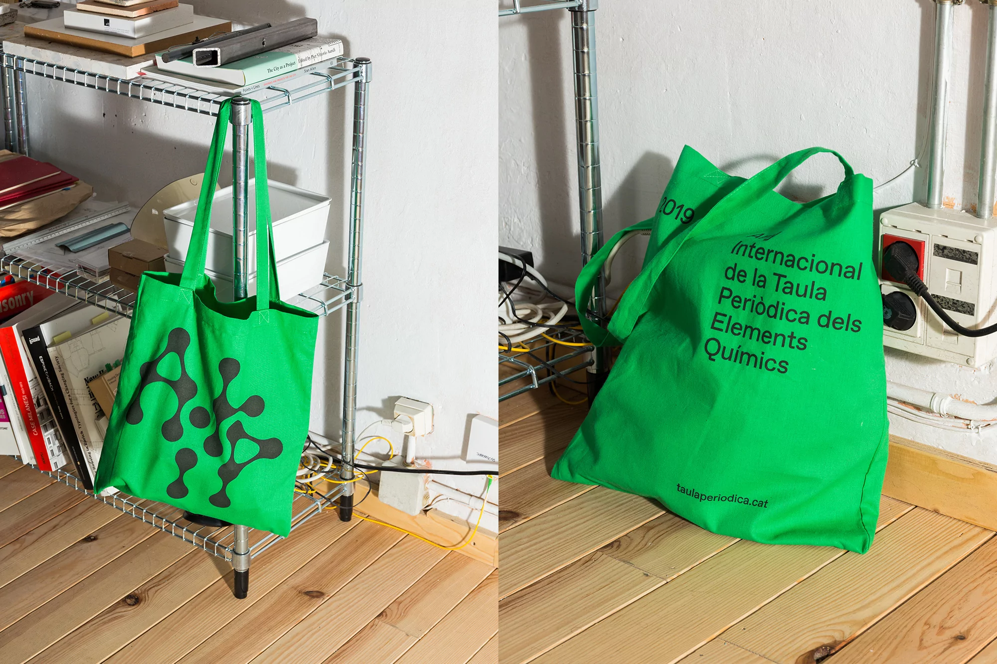 Two green tote bags with black graphics indoors, one hanging on a metal rack, the other on a wood floor near a white wall.