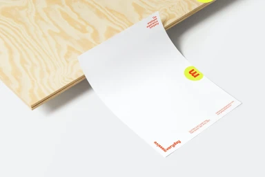 White letterhead paper resting against a light wooden panel on a clean white surface featuring red typography and a yellow circular logo.