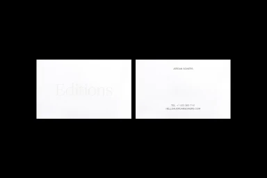 Two white business cards displayed side by side against a solid black background, featuring embossed lettering and clean typography.