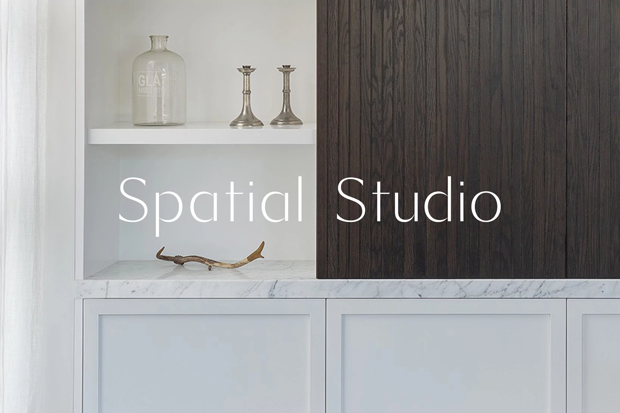 Interior design with white cabinets, dark wood panel, glass jar, silver candle holders, and marble countertop featuring a found object.