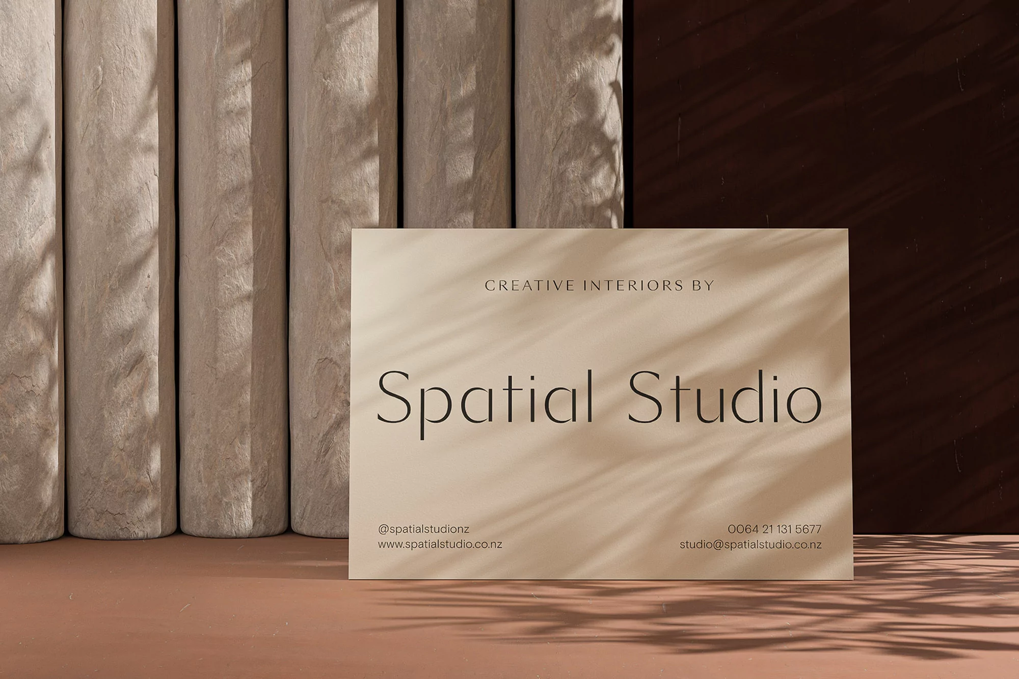 A light beige card with 'Spatial Studio' printed in bold black letters leans against rough textured columns with soft shadow effects.