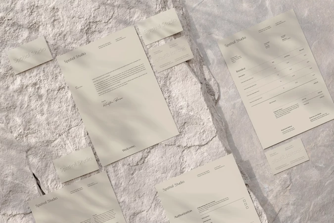Neutral-toned paper stationery mockup featuring business cards, letterhead, and invoices on a textured stone surface with soft shadows.