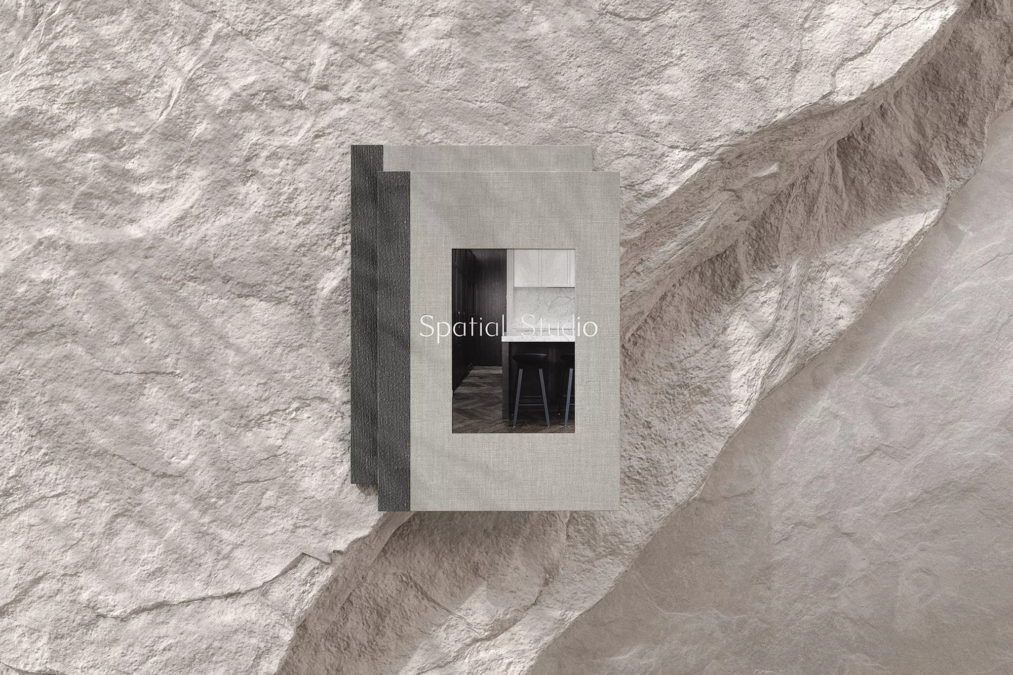 An interior design book featuring a kitchen scene is presented on a textured rock surface, creating a blend of design and natural elements.