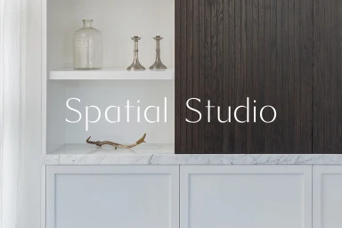 Built-in white shelving unit featuring a glass bottle, two metal candlesticks, and a small decorative branch against a dark wood cabinet panel.