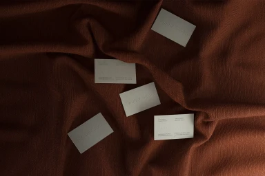 Five white business cards scattered across draped deep brown textured fabric