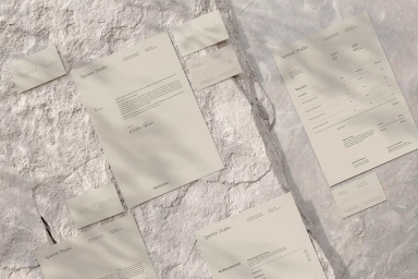 Stationery suite mockup featuring Spatial Studio branding on textured beige paper arranged over a pale stone surface.