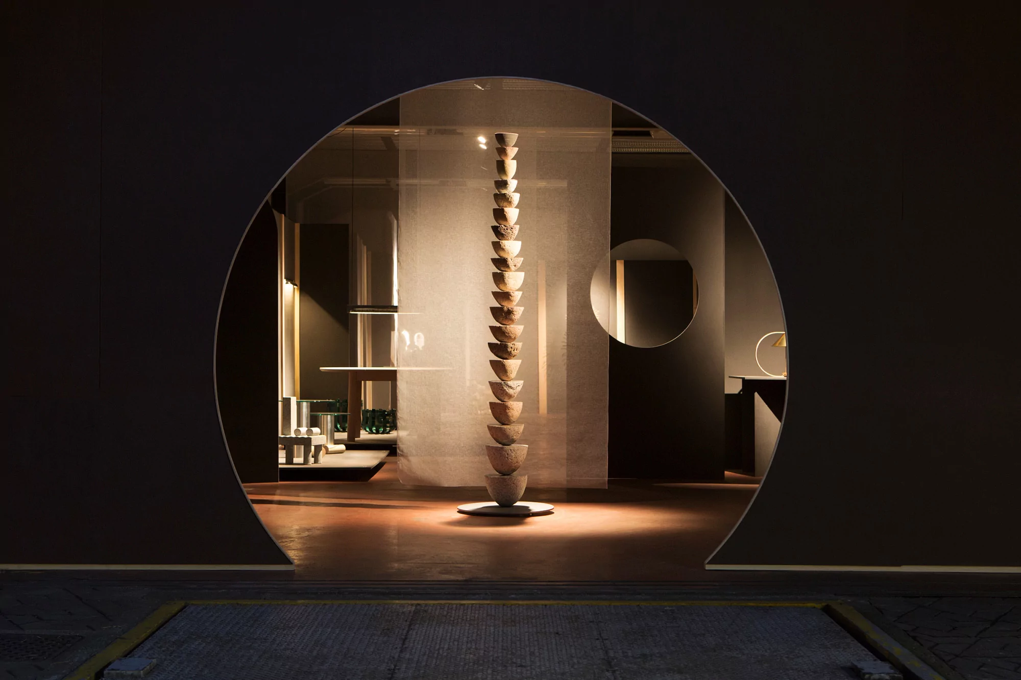 Indoor architectural studio space with a totem-like sculpture of bowls stacked on each other and displayed in a round doorway.