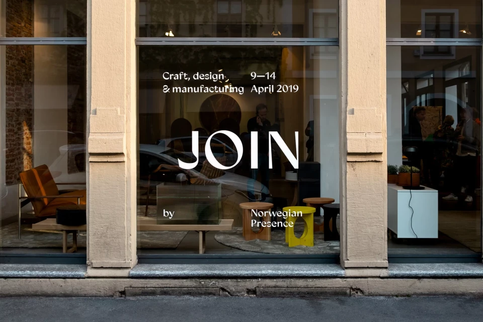 Storefront display showcasing mid-century modern furniture, including chairs, tables, and cabinets, with a person visible through the glass.