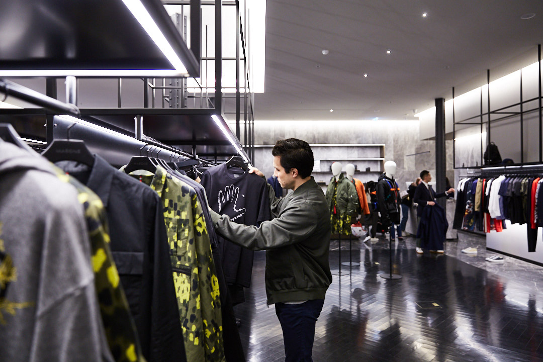 Man browses clothing rack in a modern store with track lighting and mannequins in the background; shopping and fashion concept.
