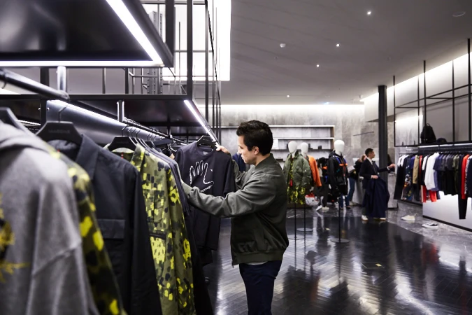 Man browses clothing rack in a modern store with track lighting and mannequins in the background; shopping and fashion concept.
