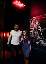 Man and woman walking out of a dimly lit venue under a red neon sign reading Juliet for Visit Victoria