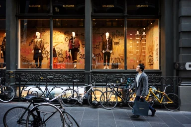 Man walking past a storefront with mannequins and parked bicycles on the city sidewalk