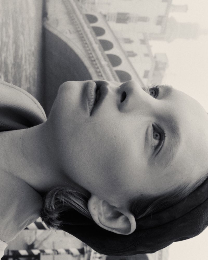 Black and white portrait of a young person looking upward with a bridge in the background, creating a serene and contemplative image.