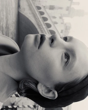 Black and white portrait of a young person looking upward with a bridge in the background, creating a serene and contemplative image.