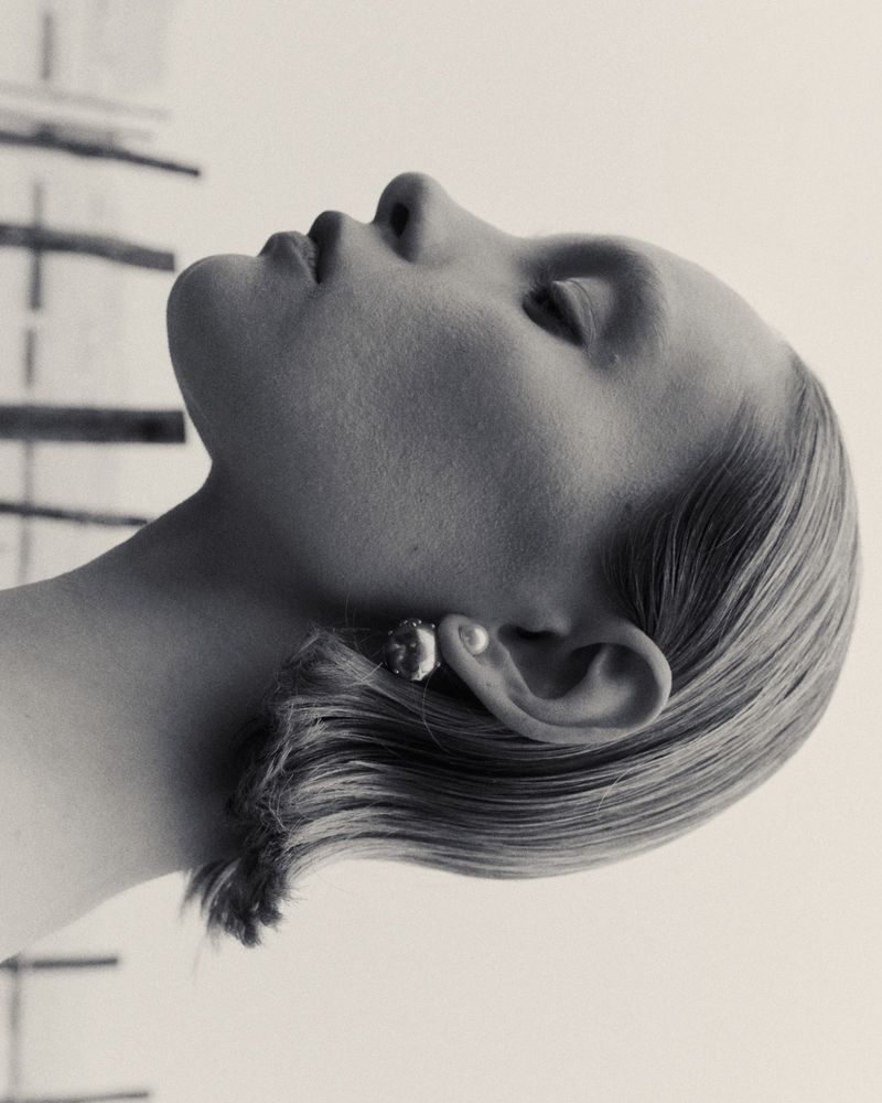 Elegant black and white portrait of a woman with short blonde hair, showcasing a round earring and smooth skin, gazing upwards in a studio.