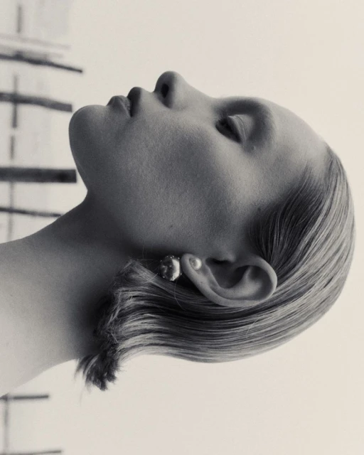 Elegant black and white portrait of a woman with short blonde hair, showcasing a round earring and smooth skin, gazing upwards in a studio.