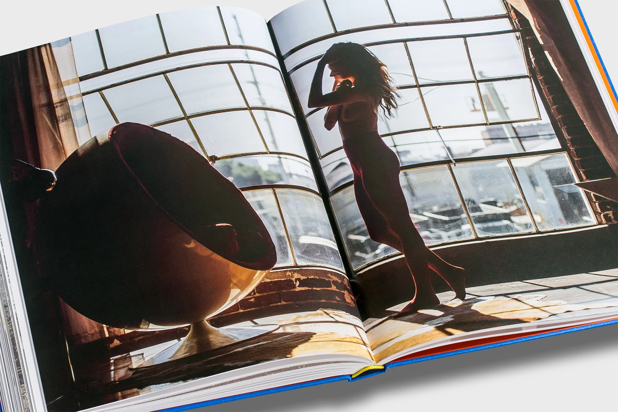 Open book showing an adult woman in front of a sunlit window with a red chair on the opposite page, shot in a photo studio.