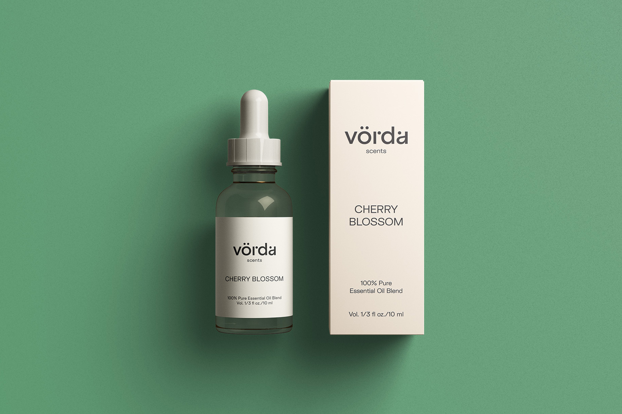 Vörda scents cherry blossom essential oil in a clear glass dropper bottle next to matching product box, set against a green background.