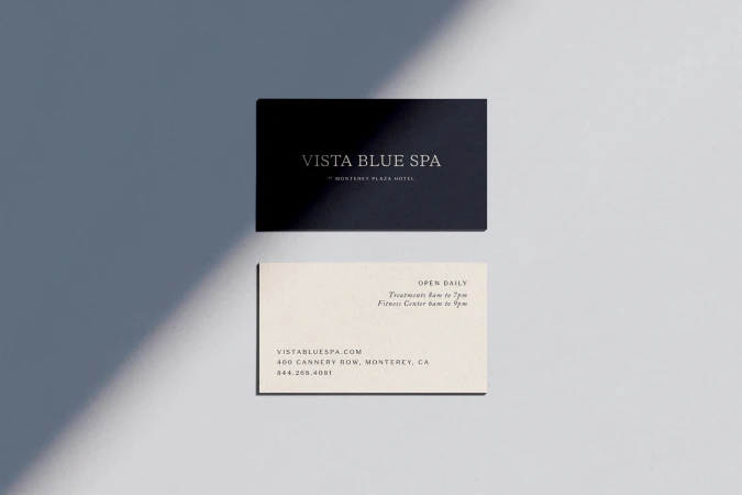 Black and cream business cards with the Vista Blue Spa logo and business information displayed against a grey background with light.