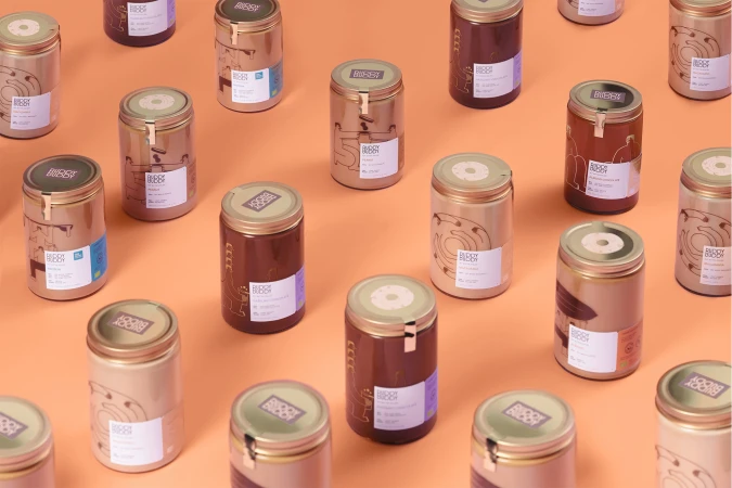 Multiple cans of Buddy Buddy spread, each with a unique flavor indicated by the label, neatly arranged on an orange background.