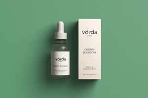 Essential oil bottle with a dropper and matching product box resting flat on a solid green background