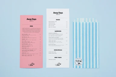 Branding materials for Away Days Brewing Co featuring printed pink and white menus alongside a blue striped paper bag on a light blue background