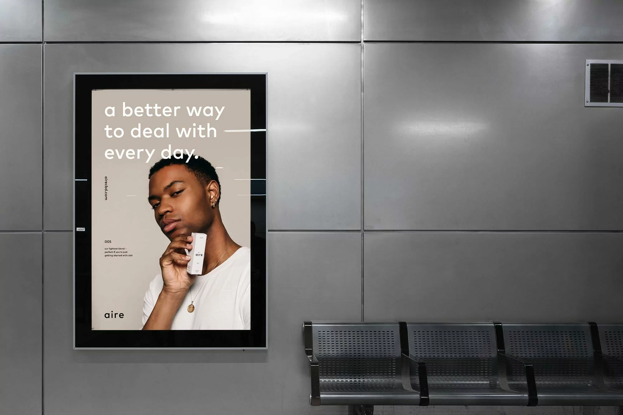 Advertisement featuring a Black male model holding a skincare product by Aire, set against a grey tiled wall with metal seating.