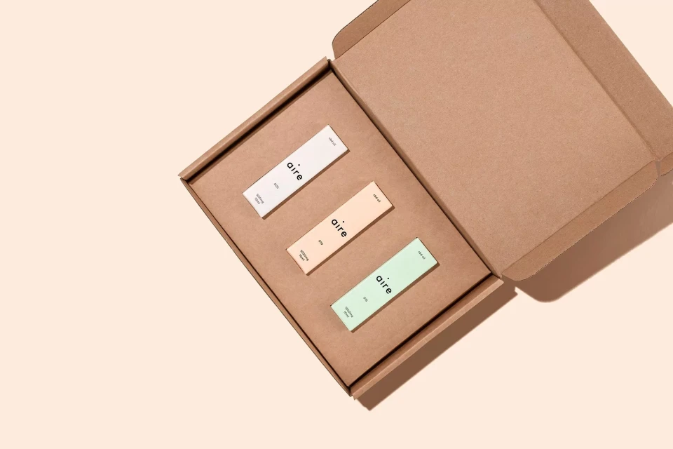 Three aire-branded product boxes displayed inside an open, unbranded cardboard box on a peach background, showcasing a minimalist aesthetic.