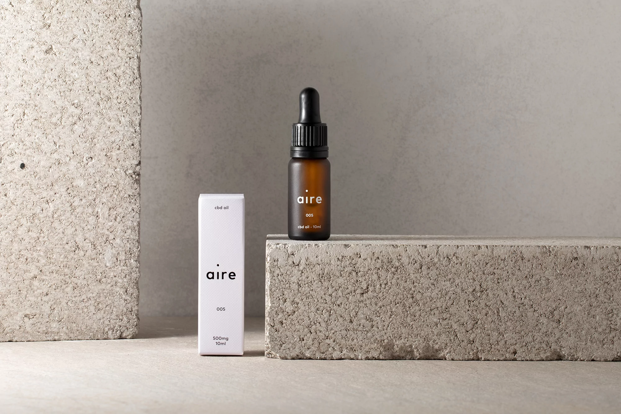 A brown glass bottle with a dropper and a white product box with the brand 'aire' are displayed against concrete blocks.
