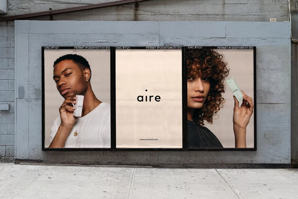 Eye-level shot of Aire CBD billboard featuring a dark-skinned male and light-skinned female holding a product box, and the brand logo.