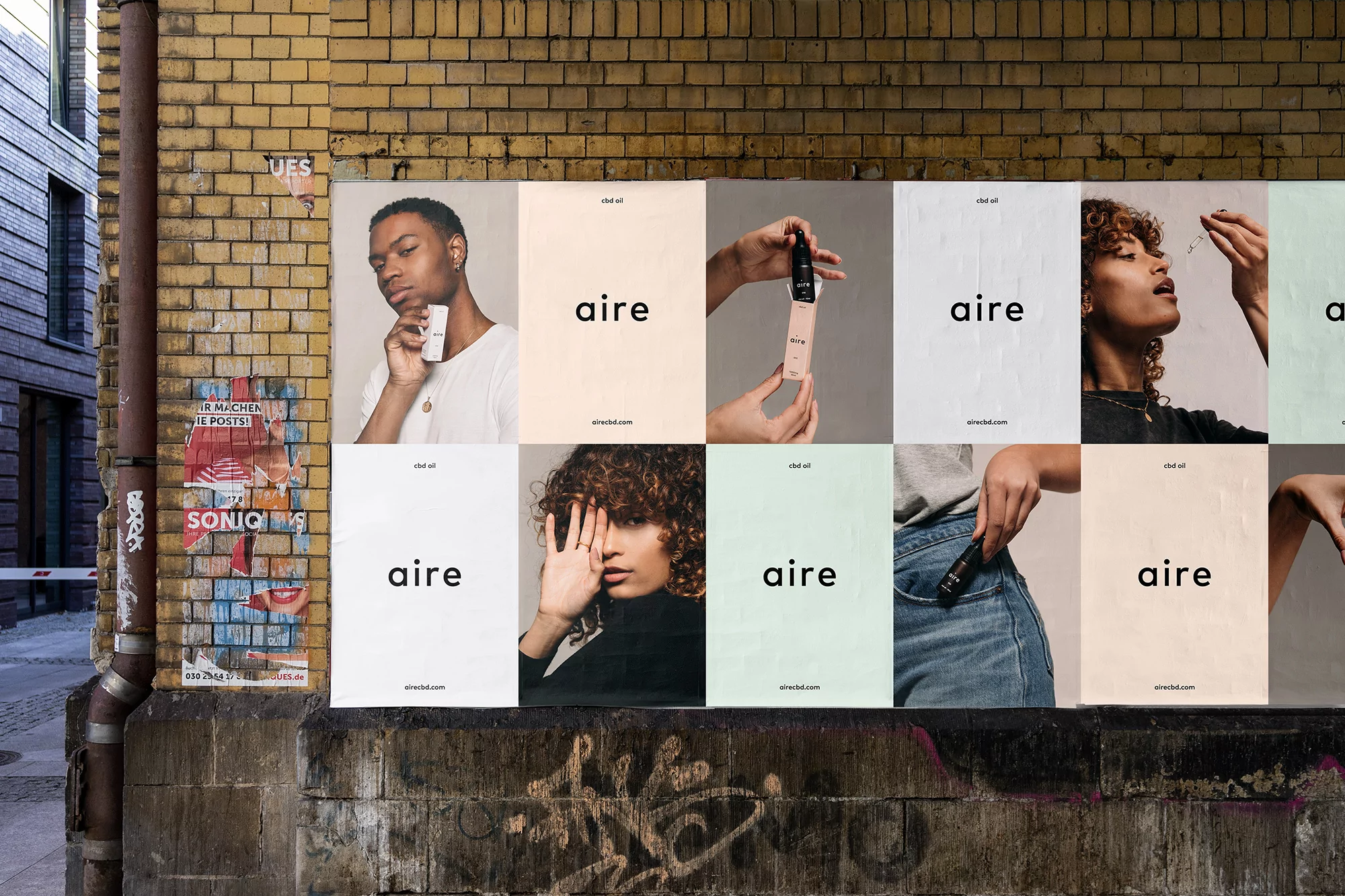Posters for Aire vital oil with diverse models displayed on brick wall in alley. Close-up shots of models and product in neutral tones.