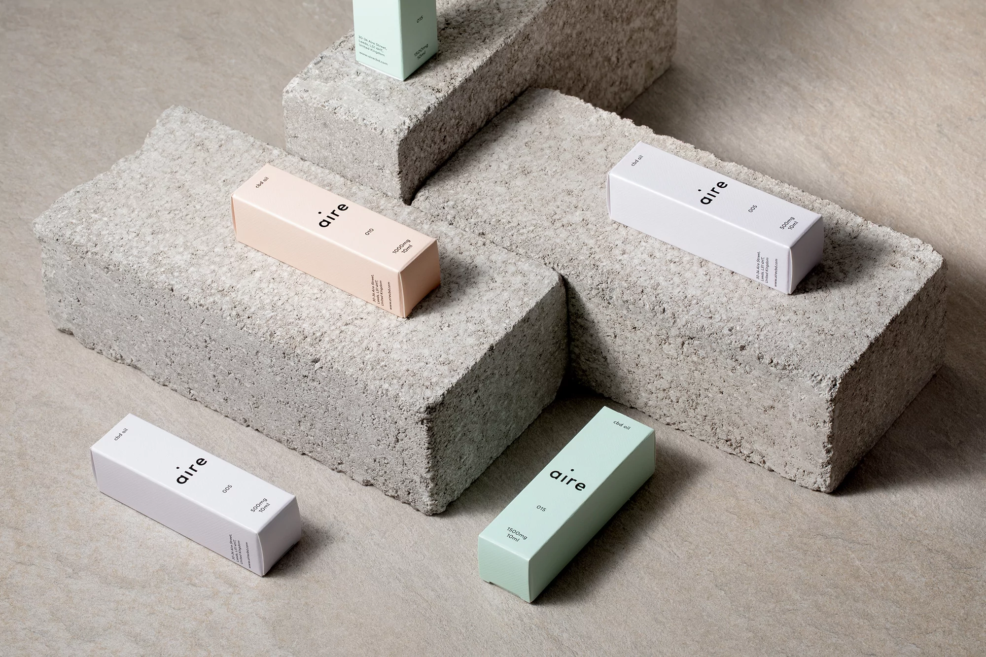 Close-up studio shot of several light-colored 'aire' branded boxes of CBD products arranged on rough concrete blocks against a beige surface.