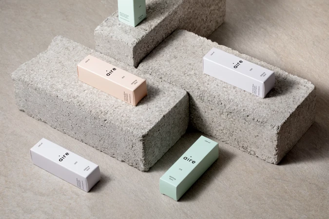 Close-up studio shot of several light-colored 'aire' branded boxes of CBD products arranged on rough concrete blocks against a beige surface.
