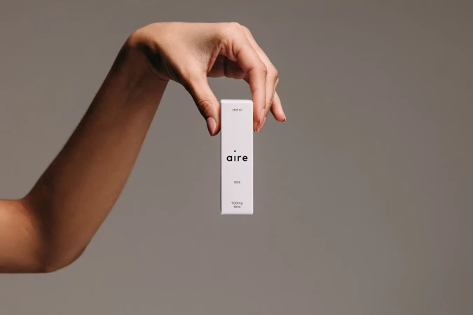 Hand holding a white Aire CBD oil product box against a neutral grey backdrop, showcasing the product in a minimalist presentation.