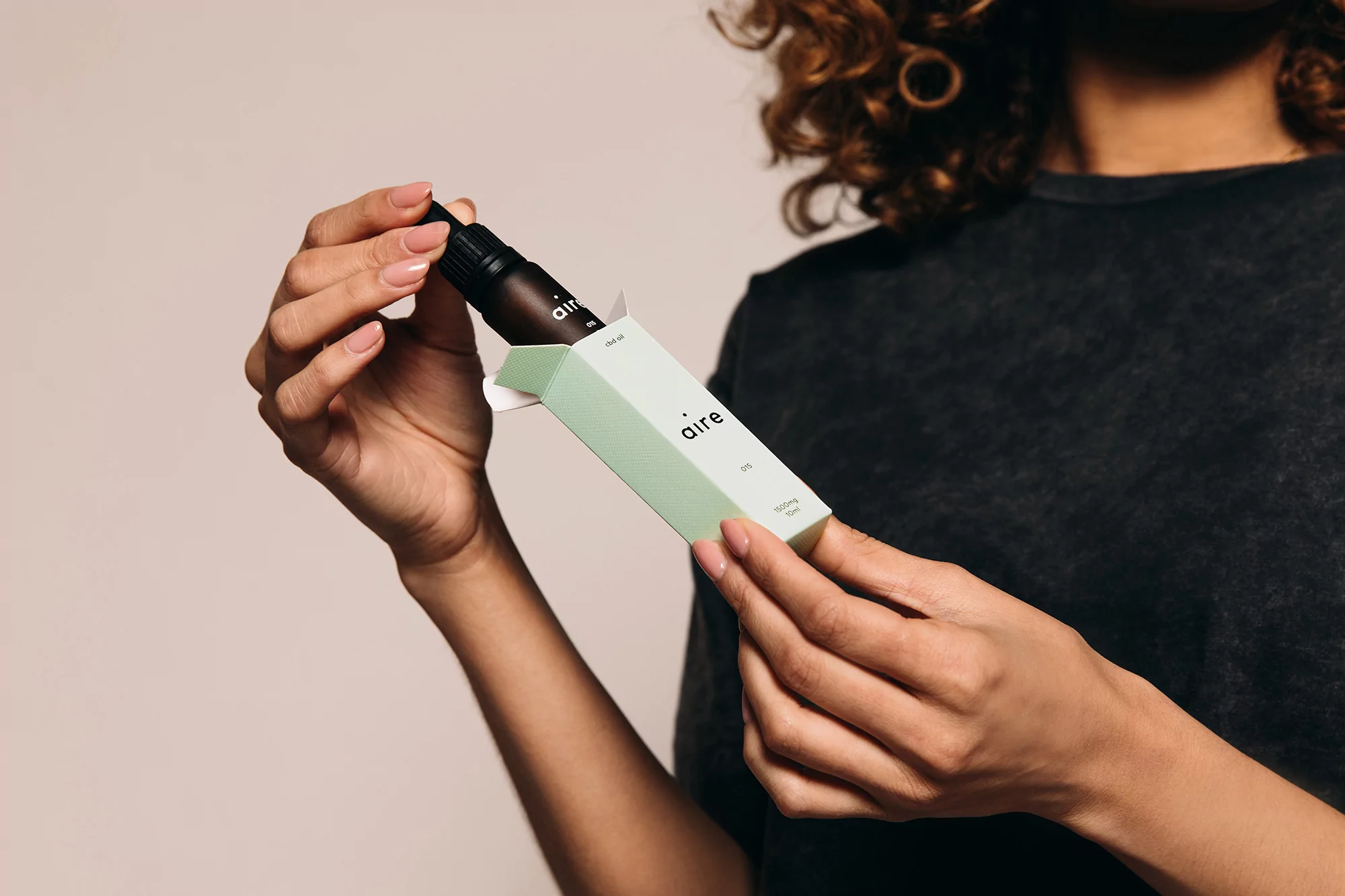 Adult female opens a box containing a small bottle against a neutral backdrop. The bottle and box feature the brand name 'aire'.