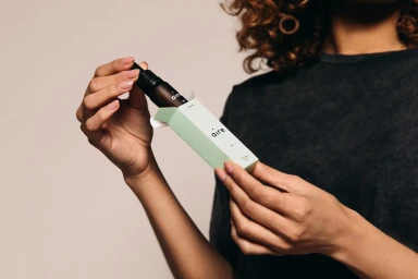 Person holding a dropper bottle coming out of a light green box with Aire branding against a plain background