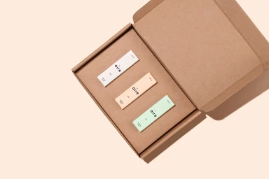Open cardboard shipping box containing three rectangular product cartons in white peach and green for Aire brand identity