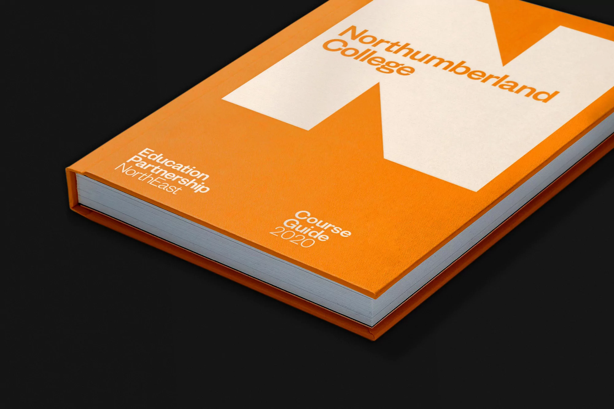 Close-up of an orange course guide book with large white typography resting on a dark surface.