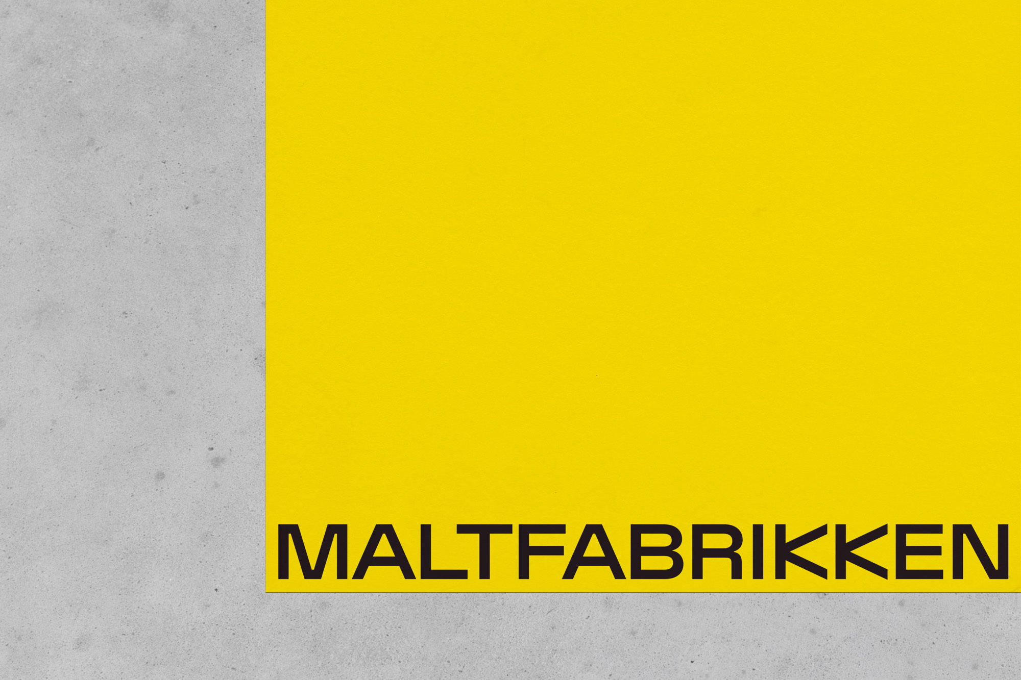 Bright yellow surface paired with a gray concrete backdrop featuring the word 'MALTFABRIKKEN' in bold black lettering along the lower edge.