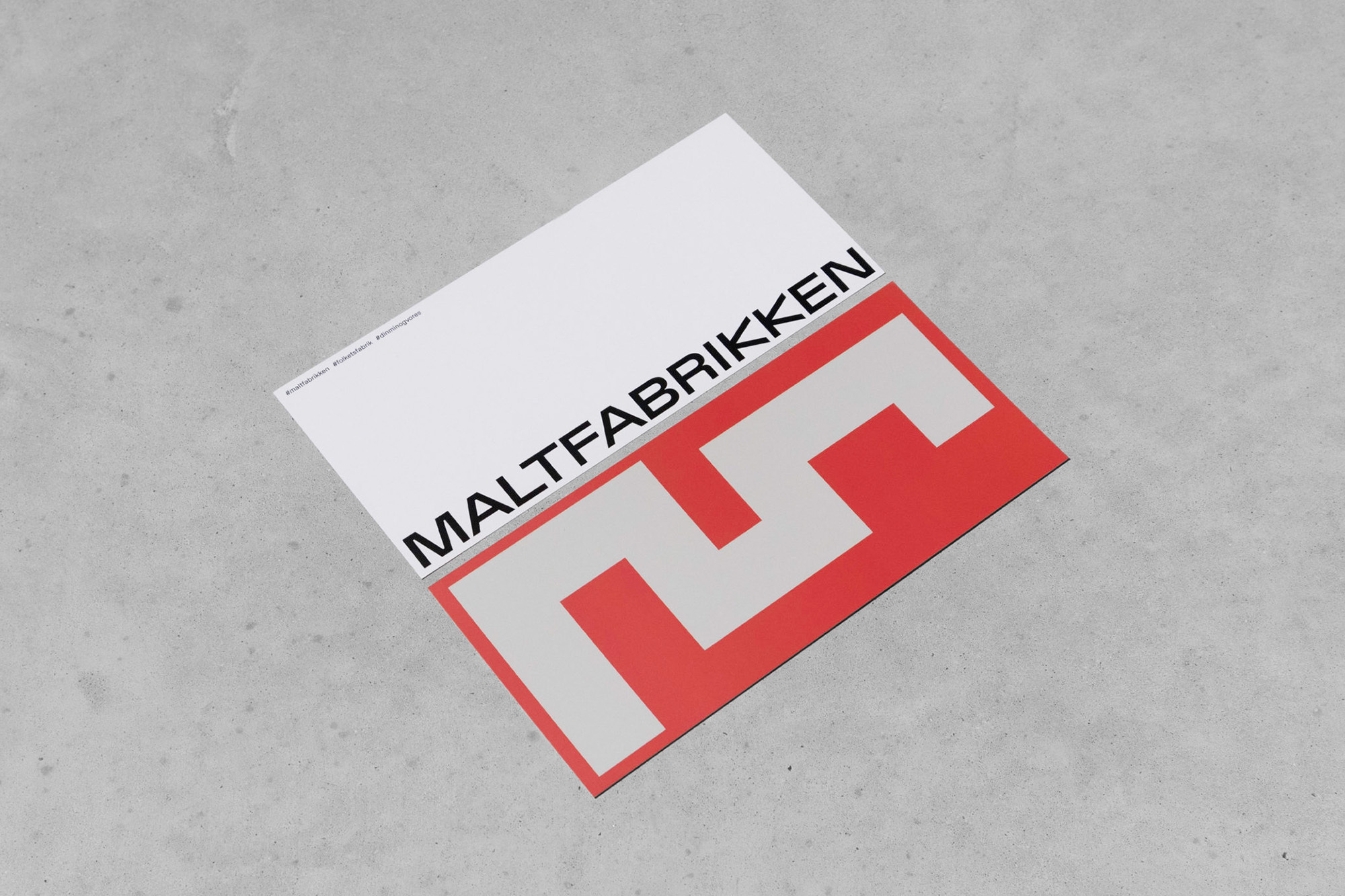Graphic design featuring the word 'Maltfabrikken' and a red square logo on a white background against a grey concrete surface.