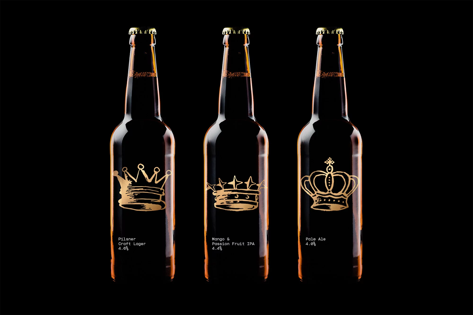 Three dark-colored beer bottles lined up with golden crown graphics and beer type text on a stark black background in a studio shot.