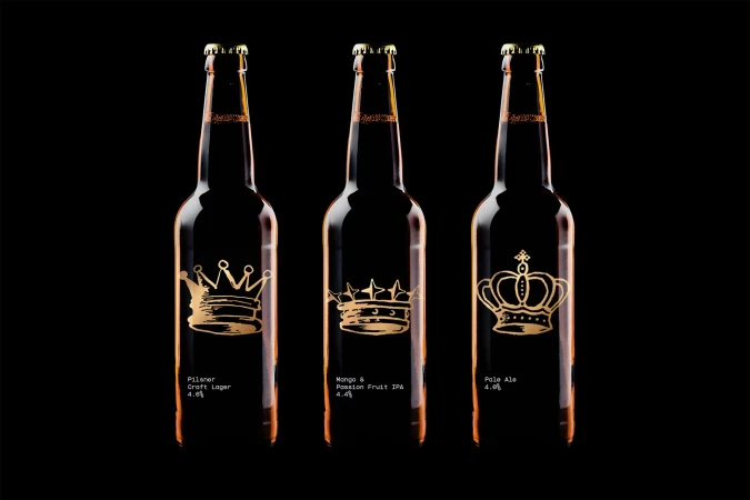 Three dark glass beer bottles featuring gold crown illustrations aligned against a solid black background.