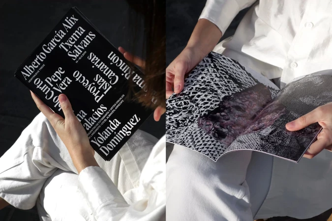Person reading a photography book with monochrome imagery, wearing a white shirt and pants, casual lifestyle, indoor setting with natural lighting.