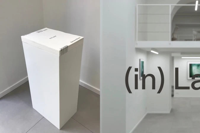 Modern art installation with a rectangular white pedestal topped with stacked paper, displayed in a bright art gallery setting.