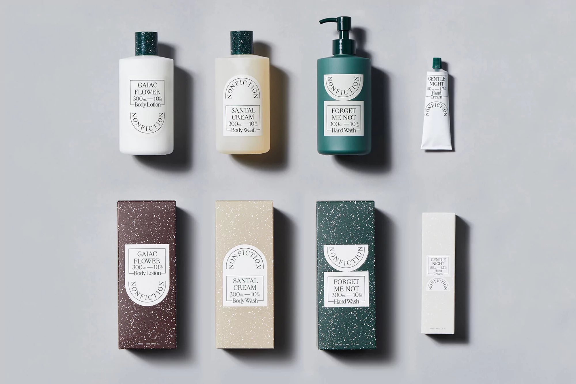Nonfiction brand product flat lay. Includes hand wash, body lotion, hand cream in white, green, and beige packaging on gray background.