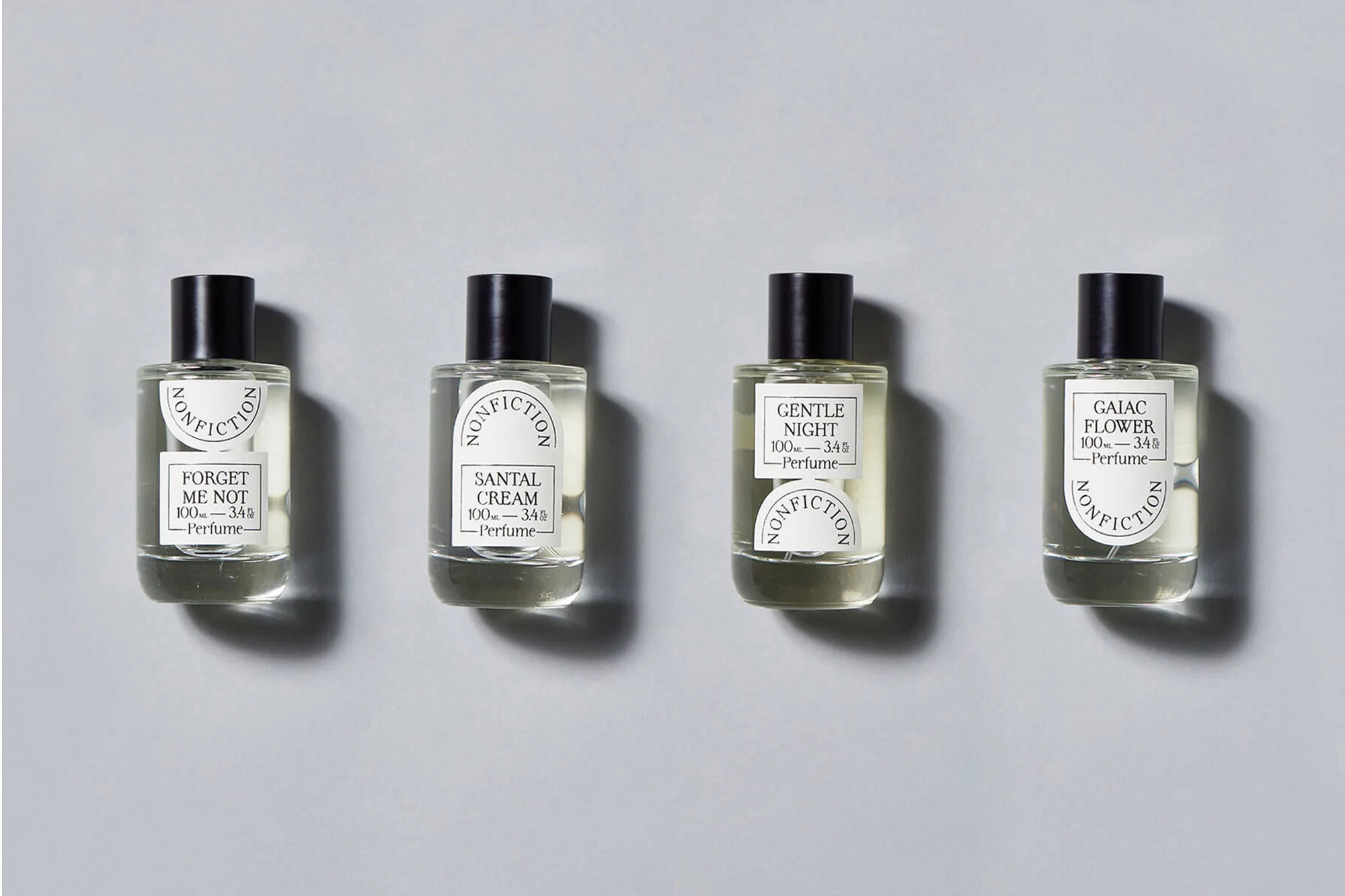 Four Nonfiction brand perfume bottles with a black cap and white label sitting side-by-side on a gray studio background, product photography.