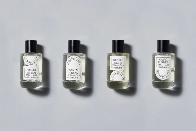 Four Nonfiction brand perfume bottles with a black cap and white label sitting side-by-side on a gray studio background, product photography.